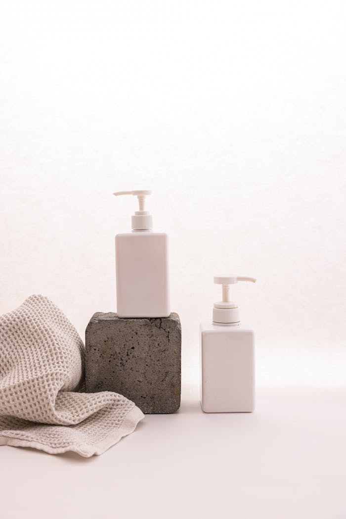 Elegant minimalist mockup of cosmetic pump bottles with concrete and fabric elements on a white background.